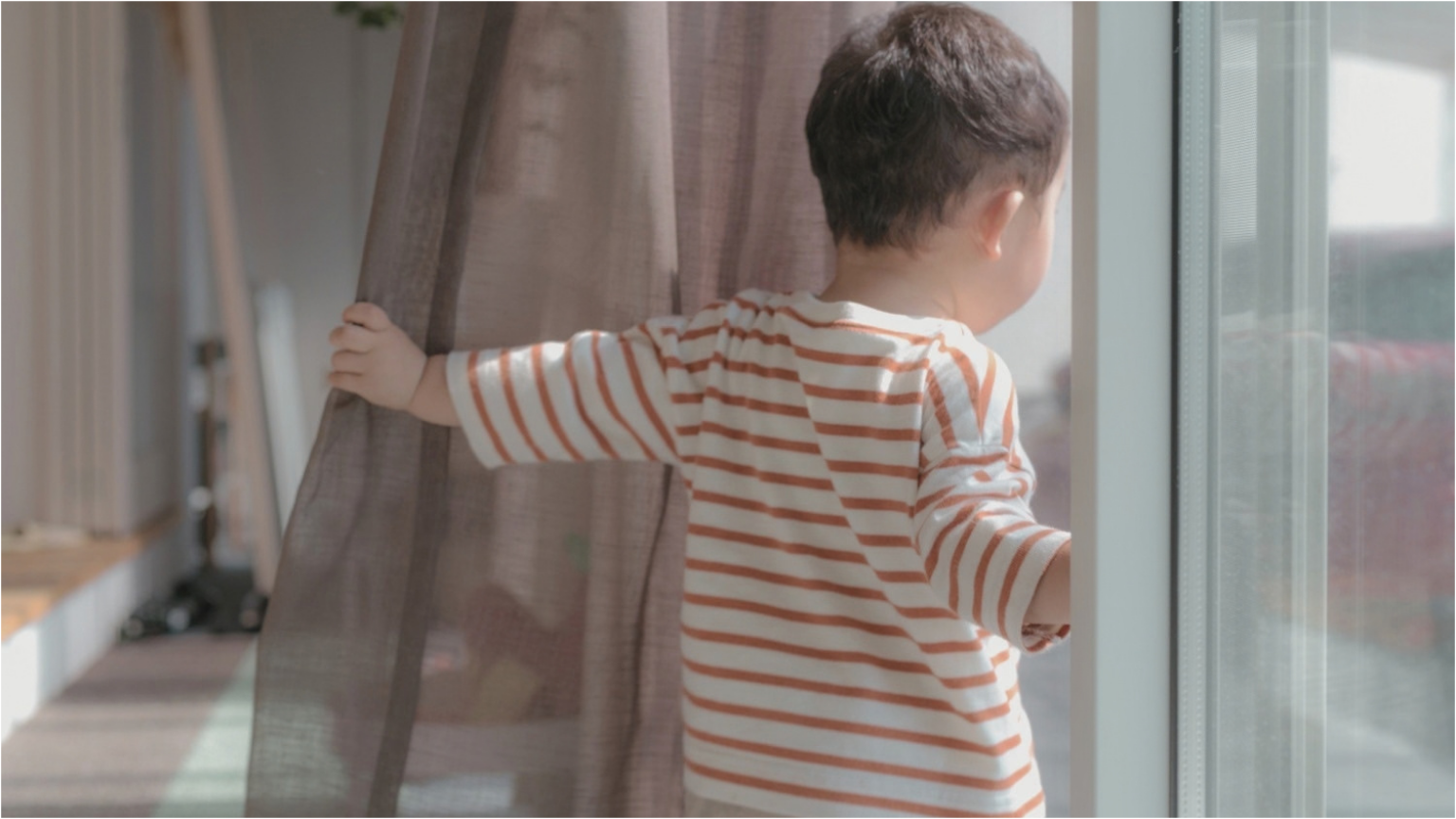 カーテン越しに外を眺める子ども